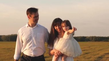 Mutlu çocukluk kavramı. Çocuk, baba ve anne güneşte çayırda oynuyorlar. Anne, baba ve küçük kız güneşin altında bir tarlada yürüyorlar. Mutlu, genç bir aile. Mutlu aile kavramı.