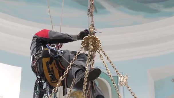 Промышленный альпинист на лестнице готовит веревку для подъемного оборудования. рабочий в защитном шлеме вяжет узел на веревке . — стоковое видео