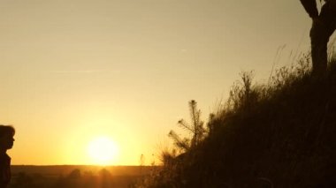 Macera ve seyahat kavramı. Gezgin adam, bir kadının elini bir gezginin tepeye tırmanmasına uzatır. Turistler gün batımında el ele tutuşarak dağa tırmanırlar. iş adamlarının takım çalışması