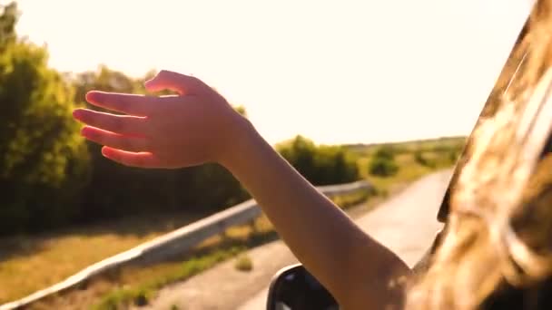Chica con el pelo largo está sentado en el asiento delantero del coche, estirando su brazo por la ventana y la captura de resplandor de puesta de sol — Vídeos de Stock
