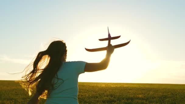 Gelukkig meisje rent met een speelgoedvliegtuigje op een veld bij zonsondergang. kinderen spelen speelgoed vliegtuig. tiener droomt van vliegen en piloot worden. Het meisje wil piloot en astronaut worden. Langzame beweging — Stockvideo