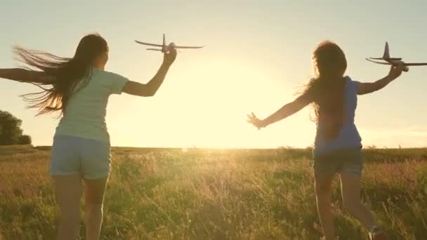 Mutlu çocukluk kavramı. Uçma hayalleri. Gün batımında iki kız bir oyuncak uçakla oynuyor. Güneşin arka planındaki çocuklar ellerinde bir uçakla. Uçakta oynayan çocukların silueti — Stok video