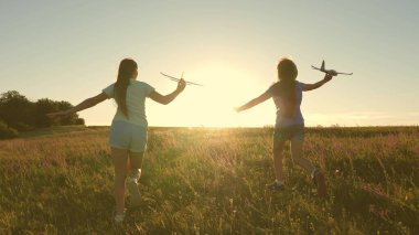 Mutlu çocukluk kavramı. Uçma hayalleri. Gün batımında iki kız bir oyuncak uçakla oynuyor. Güneşin arka planındaki çocuklar ellerinde bir uçakla. Uçakta oynayan çocukların silueti