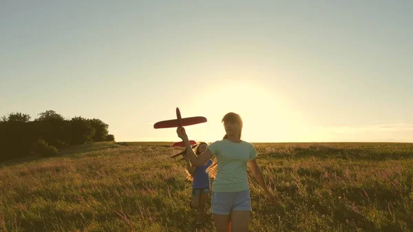 Uçma hayalleri. Mutlu çocukluk kavramı. Gün batımında iki kız bir oyuncak uçakla oynuyor. Güneşin arka planındaki çocuklar ellerinde bir uçakla. Uçakta oynayan çocukların silueti. — Stok fotoğraf