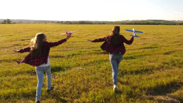 Ellerinde bir uçakla çayırdaki çocuklar. Uçma hayalleri. Mutlu bir çocukluk kavramı. İki kız sahada oyuncak bir uçakla oynar. Uçakta oynayan çocukların silueti. — Stok fotoğraf