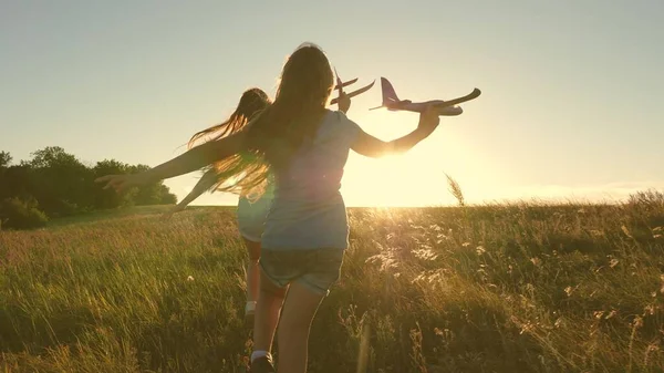 Concepto de infancia feliz. Sueños de volar. Dos chicas juegan con un avión de juguete al atardecer. Niños en el fondo del sol con un avión en la mano. Silueta de niños jugando en avión — Foto de Stock