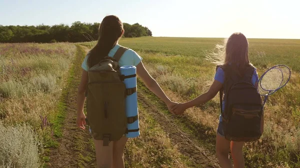 Teamwork toeristen tieners. Vrouwelijke reizigers lopen over een weg op het platteland. Gelukkig wandelmeisje in het zomerpark. Gelukkige meisjes reizigers gaan met rugzakken in het veld. tiener meisje avonturen op vakantie. — Stockfoto