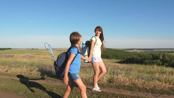 Teamwork toeristen tieners. Vrouwelijke reizigers lopen over een weg op het platteland. Gelukkig wandelmeisje in het zomerpark. Gelukkige meisjes reizigers gaan met rugzakken in het veld. tiener meisje avonturen op vakantie. — Stockfoto