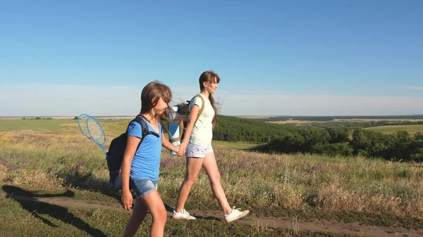 Teamwork toeristen tieners. Vrouwelijke reizigers lopen over een weg op het platteland. Gelukkig wandelmeisje in het zomerpark. Gelukkige meisjes reizigers gaan met rugzakken in het veld. tiener meisje avonturen op vakantie. — Stockfoto