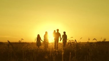 Mutlu çocukluk kavramı. Mutlu büyük aile gün batımında tarlada yürüyor. Ebeveynler ve üç çocuk akşam parkta yürürler. Tatil ve seyahat. Ağır çekim. Mutlu aile kavramı