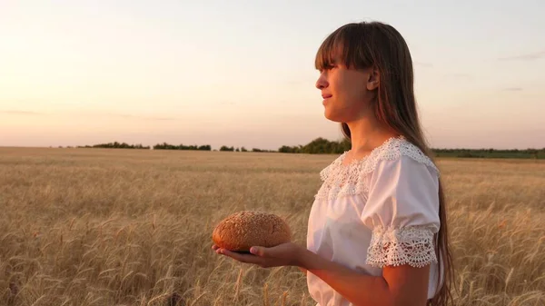 Délicieux pain dans les mains porte une jeune belle femme sur un champ de blé. pain dans les mains d'une jeune fille sur un champ de blé dans les rayons du coucher du soleil. savoureux pain sur les paumes . — Photo