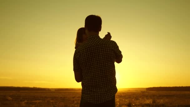 Concetto di infanzia felice. Papà sta ballando con un bambino tra le braccia in campo al sole. padre e figlioletta volteggiano nella danza al tramonto. bambino felice gioca con suo padre al tramonto. concetto di a — Video Stock