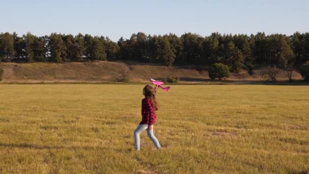 Conceito de infância feliz. criança lança um avião para o céu e sorri. Um adolescente sonha em voar e se tornar um piloto ou um astronauta. Menina feliz corre com um brinquedo de avião no campo . — Vídeo de Stock