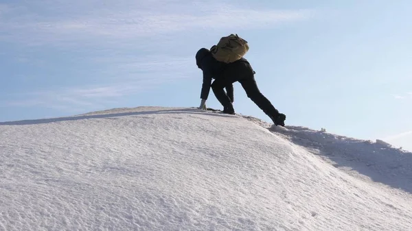 Der Mensch rückt zu seinem Erfolg an die Spitze. Bergsteiger erklimmt schneebedeckten Berg in Strahlen der strahlenden Sonne. Tourist macht Aufstieg nach oben auf dem Hintergrund des schönen Himmels. — Stockfoto