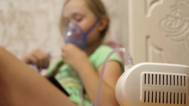 Tabletli çocuk hasta ve astım spreyinden nefes alıyor. Yakın plan. Hastanede yüzünde solunum maskesiyle tedavi edilen küçük bir kız. Yürümeye başlayan çocuk, solunum buharı soluyarak grip tedavisi görüyor..