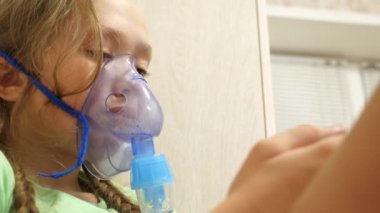 Tabletli çocuk hasta ve astım spreyinden nefes alıyor. Yakın plan. Hastanede yüzünde solunum maskesiyle tedavi edilen küçük bir kız. Yürümeye başlayan çocuk, solunum buharı soluyarak grip tedavisi görüyor..