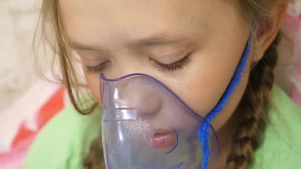 El niño con el comprimido está enfermo y respira a través de un inhalador. Primer plano. niña pequeña tratada con una máscara de inhalación en su cara en el hospital. El niño pequeño trata la gripe inhalando vapor de inhalación . — Vídeo de stock