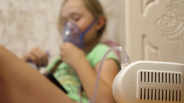 El niño con el comprimido está enfermo y respira a través de un inhalador. Primer plano. niña pequeña tratada con una máscara de inhalación en su cara en el hospital. El niño pequeño trata la gripe inhalando vapor de inhalación . — Vídeo de stock