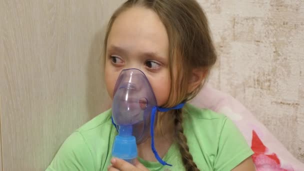 El niño con el comprimido está enfermo y respira a través de un inhalador. Primer plano. niña pequeña tratada con una máscara de inhalación en su cara en el hospital. El niño pequeño trata la gripe inhalando vapor de inhalación . — Vídeos de Stock