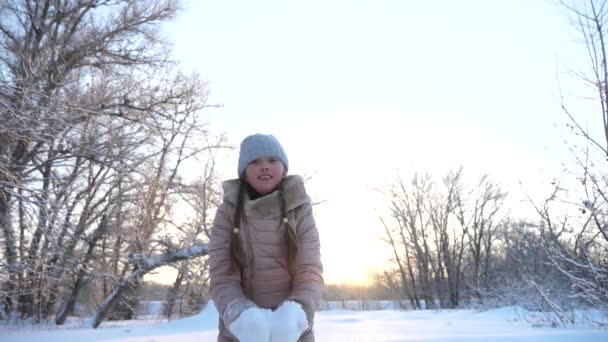 Concetto di infanzia felice. bambino gettando fiocchi di neve per la parte superiore gioisce e sorride nel parco invernale. Al rallentatore. Ragazza gioca in inverno durante le vacanze di Natale. Il concetto di una famiglia felice . — Video Stock