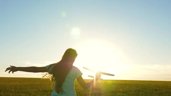 Lycklig flicka springer med ett leksaksplan på ett fält i solnedgångens sken. Barn leker leksaksflygplan. Tonåringen drömmer om att flyga och bli pilot. Flickan vill bli pilot och astronaut. Långsamma rörelser — Stockfoto