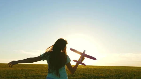 Chica feliz corre con un avión de juguete en un campo en la luz del atardecer. niños juegan juguete avión. adolescente sueña con volar y convertirse en piloto. la chica quiere convertirse en piloto y astronauta. Movimiento lento — Foto de Stock