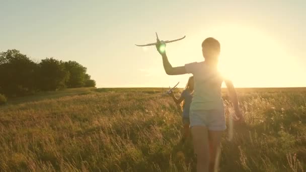 Niños en el fondo del sol con un avión en la mano. Sueños de volar. Concepto de infancia feliz. Dos chicas juegan con un avión de juguete al atardecer. Silueta de niños jugando en el avión — Vídeos de Stock