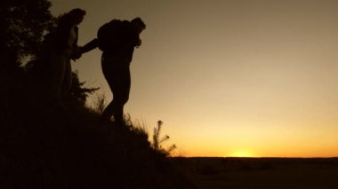seyahat ve macera konsepti. Erkek gezgin ve dişi gezgin tepenin üstünden inerler. İş adamlarından oluşan takım çalışması. Turistler gün batımında birbiri ardına dağdan inerler..