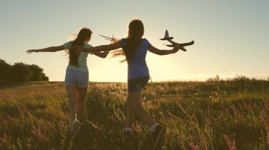 Happy childhood concept. Dreams of flying. Two girls play with a toy plane at sunset. Children on background of sun with an airplane in hand. Silhouette of children playing on plane clipart