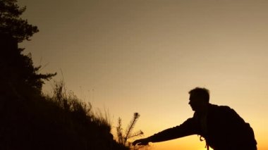 seyahat ve macera konsepti. Turistler gün batımında el ele tutuşarak dağa tırmanırlar. Dişi gezgin, tepeye tırmanmaya yardım eden bir erkek yolcunun elini tutuyor. İş ortaklarının takım çalışması.