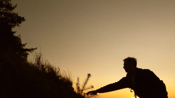 Travel and adventure concept. Tourists climb the mountain at sunset, holding hands. female traveler holds the hand of a male traveler helping to climb top of hill. team work of business partners. — Stock Video