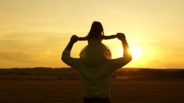 Baba ve küçük kızı omuzlarında yürüyüp gün batımını izliyorlar. Mutlu çocukluk kavramı. Mutlu aile kavramı. Ailesi, babası küçük çocuğuyla parkta oynuyor..