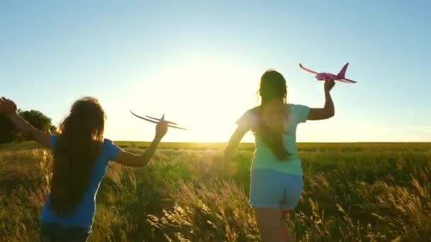 Мрії про політ. Щаслива концепція дитинства. Дві дівчини грають з іграшковим літаком на заході сонця. Діти на фоні сонця з літаком в руці. Силует дітей, які грають у літаку — стокове відео