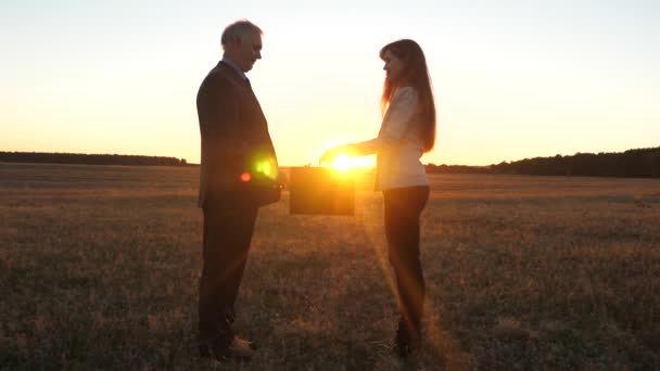 La mujer de negocios pasa el portafolio con los documentos al empresario. granjeros hombre y mujer hicieron un trato. hombre de negocios y mujer de negocios estrechando las manos en el resplandor de la puesta del sol . — Vídeos de Stock