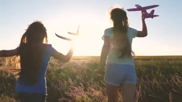 飛行機で遊んでいる子供たちのシルエット。空飛ぶ夢。幸せな子供時代のコンセプト。2人の女の子が日没時におもちゃの飛行機で遊ぶ。太陽を背景に飛行機を手にした子供たち. — ストック動画