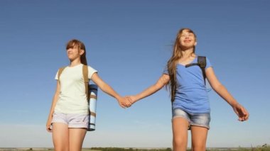 Turizm ve seyahat kavramı. Kızlar, kadın gezginler mavi gökyüzünün arka planında el ele tutuşurlar. Takım çalışması turistleri. Kadın gezginler arazide yürür. Otlakçı kızlar yazın çayırda.