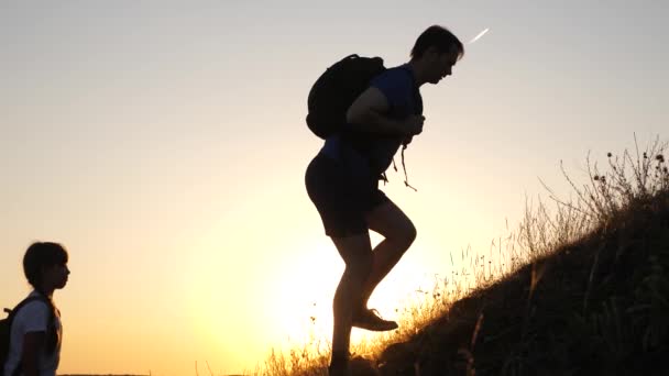 Travelers with children travel at sunset. father holds out his hand helping children climb mountain. dad, children and mom with backpacks travel climb mountain in the sun. tourist teamwork — Stock Video