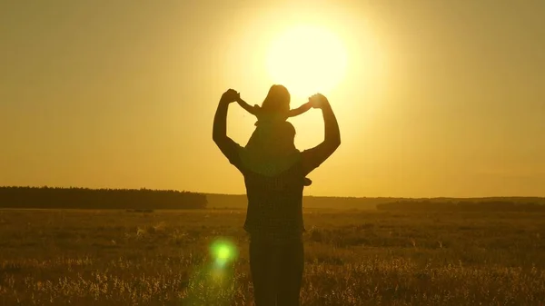 Papà porta l'amato bambino sulle spalle che cammina intorno al campo al tramonto. Un bambino con genitore cammina la sera al tramonto del sole. Figlia che cavalca con papa 'sulle spalle nel parco. Rallentatore . — Foto Stock