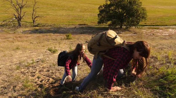 Reisenden Teamwork. Touristen mit Rucksäcken helfen sich gegenseitig den Berg hinauf. Backpacker helfen sich gegenseitig den Berg hinauf. Touristenfamilie mit Kindern unterwegs bei Sonnenuntergang. — Stockfoto