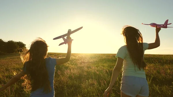 Dreams of flying. Happy childhood concept. Two girls play with a toy plane at sunset. Children on background of sun with an airplane in hand. Silhouette of children playing on the plane