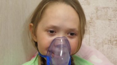 Tabletli çocuk hasta ve astım spreyinden nefes alıyor. Yakın plan. Hastanede yüzünde solunum maskesiyle tedavi edilen küçük bir kız. Yürümeye başlayan çocuk, solunum buharı soluyarak grip tedavisi görüyor..
