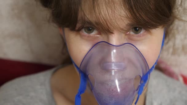 Una mujer con una máscara azul del hospital. Inhala vapores desde el tracto respiratorio hacia los pulmones. Tratamiento para la tos. Una chica enferma con una máscara inhaló una botella de spray. Primer plano — Vídeos de Stock