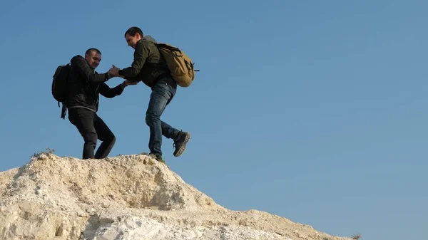 Trabalho de equipa de pessoas de negócios. turistas dão a mão uns aos outros, subindo para o topo da colina. equipe de viajantes do sexo masculino vai para a vitória e sucesso. dois alpinistas escalam um após o outro na rocha branca . — Fotografia de Stock