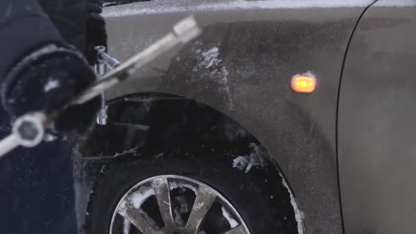 Man höjer bilen jack på väg. man förändras ratten i bilen. reservhjul i vintern på väg i en snöstorm och snöfall. Uppdelning av bil, hjulbyte. — Stockvideo