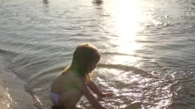 Bebek suya su sıçratıyor. Su sıçratıyor. Sevimli çocuk kumsalda mutlu bir şekilde oynuyor. Mutlu çocuk gün batımında bir nehirde, denizde, gölde banyo yapar. Mutlu çocukluk kavramı.