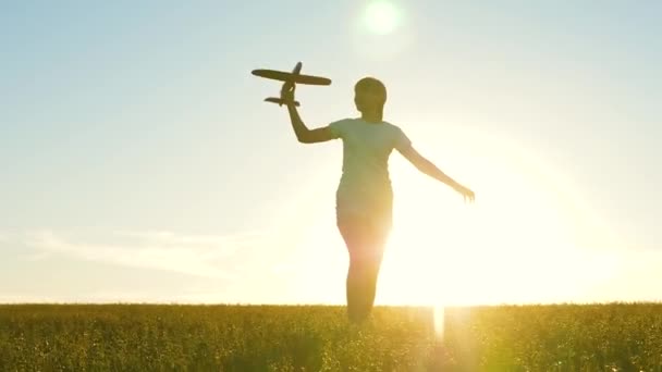 Mutlu kız gün batımında oyuncak bir uçakla sahada koşuyor. Çocuklar oyuncak uçak oynuyorlar. Gençler uçmayı ve pilot olmayı hayal eder. Kız pilot ve astronot olmak istiyor. Yavaş çekim — Stok video