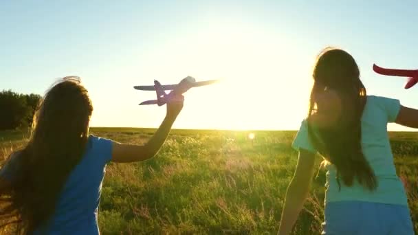 幸せな子供時代のコンセプト。空飛ぶ夢。2人の女の子が日没時におもちゃの飛行機で遊ぶ。手に飛行機で太陽を背景に子供たち。飛行機で遊ぶ子供たちのシルエット — ストック動画