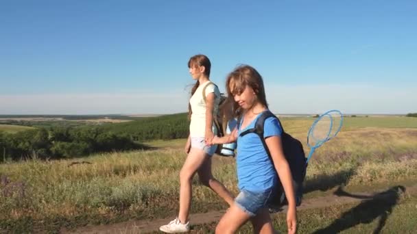 チームワークの観光客10代女性の旅行者は田舎の道路を歩く。夏の公園で幸せなハイカーの女の子。幸せな女の子の旅行者の分野でバックパックで行く。休暇で10代の女の子の冒険. — ストック動画