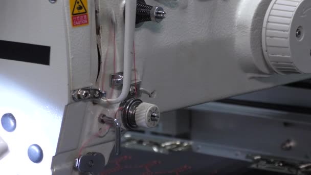 Een naaimachine naait met een rode draad. Close-up van de draad. Kleding maken in de winkel. Vervaardiging van deksels en kleding — Stockvideo