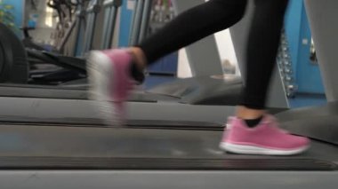 Spor yaşam tarzı konsepti. Spor ayakkabılı kızın bacakları koşu bandına kadar uzanıyor. Yakın plan. Yürürken bacak kaslarını güçlendiriyor. Kardiyo yüklemesi. Spor salonundaki kadın yürüyüşe çıkıyor. Spor salonunda kilo kaybı.